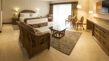 Une chambre d’hôtel avec un grand lit, un canapé, une table à manger avec des chaises, une télévision et un bureau avec des tiroirs.