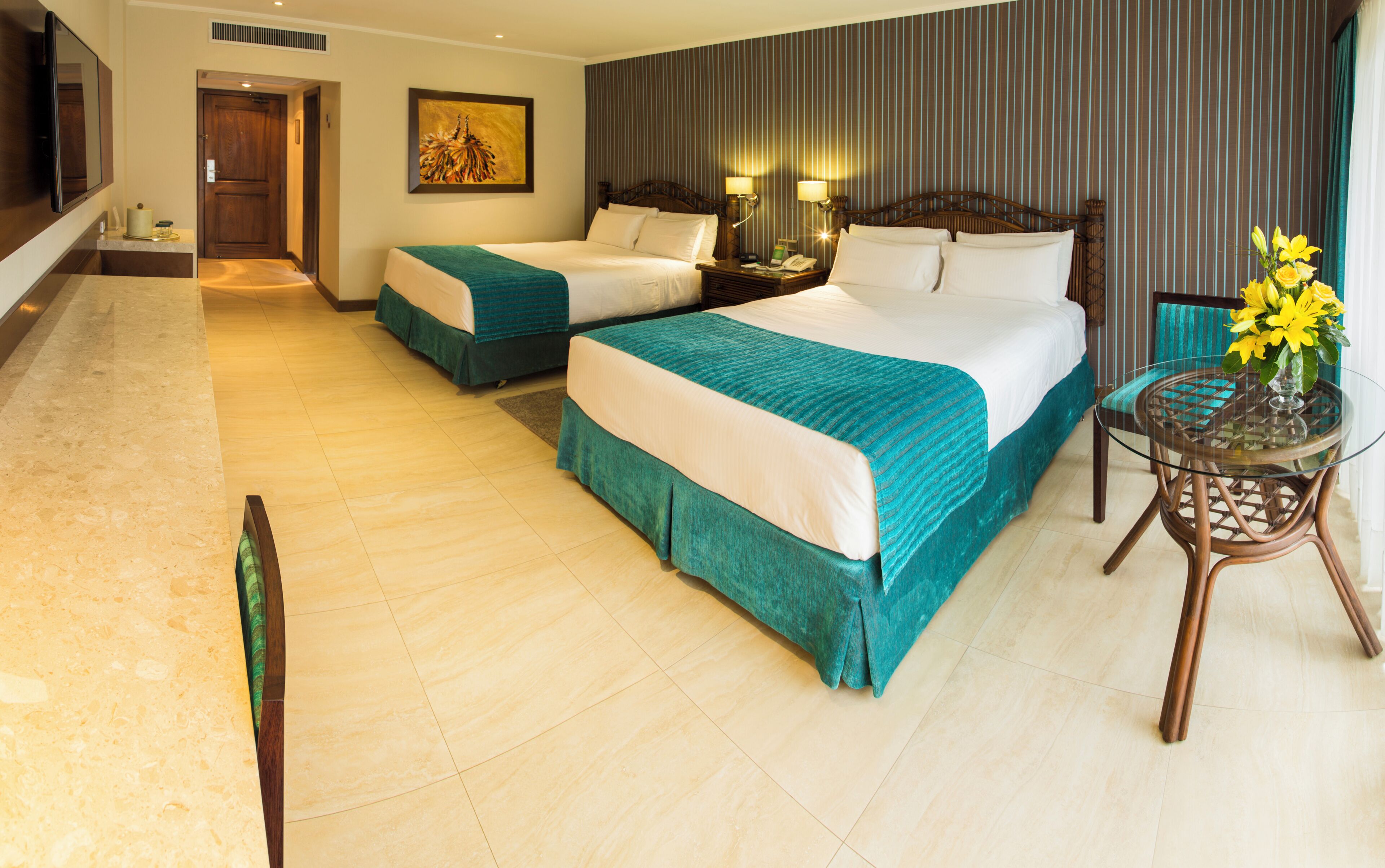 A hotel room with two beds, a sitting area with a glass table, and a view of the hallway.