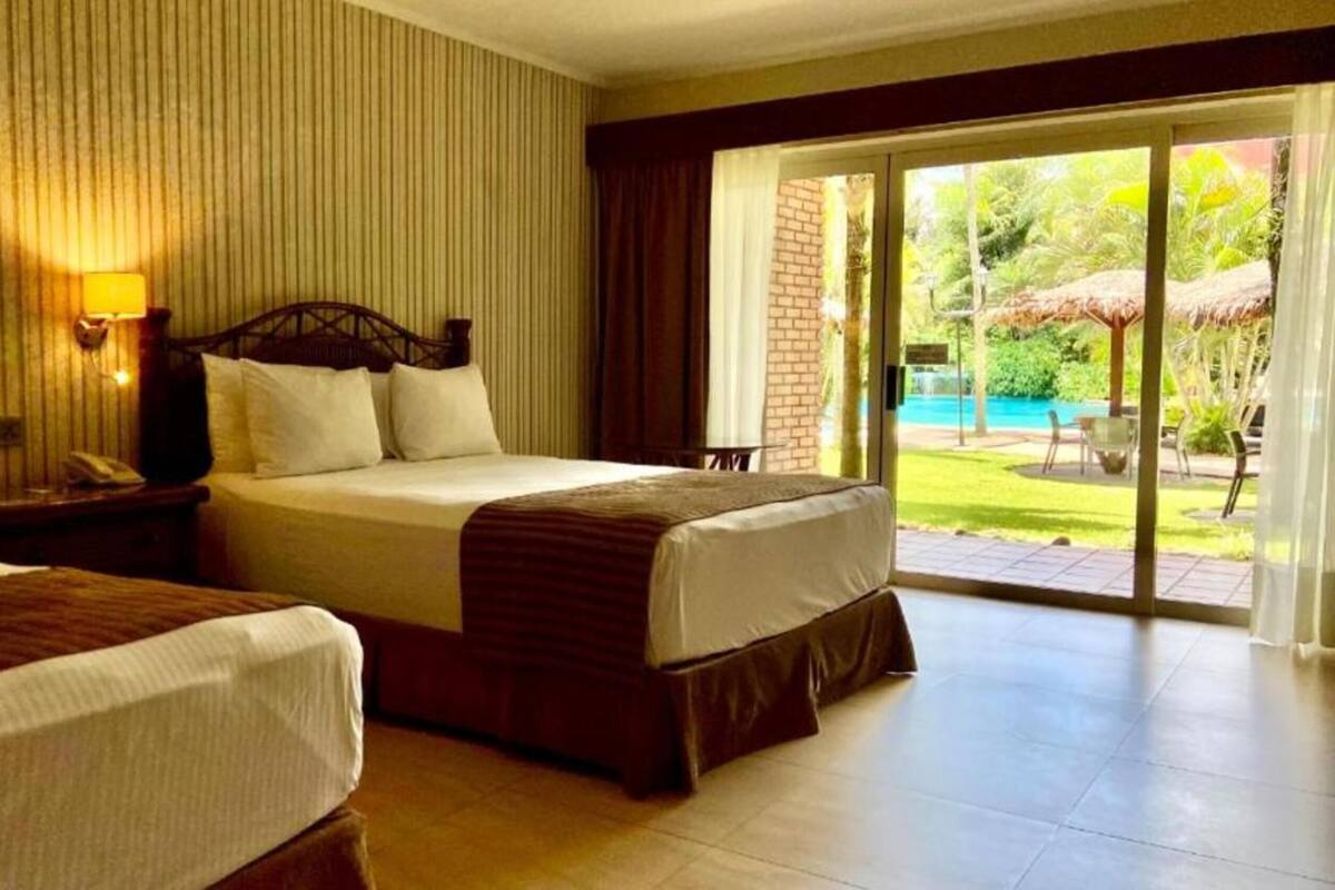 A hotel room with two beds, a large sliding glass door leading to a pool area, and a brick wall.