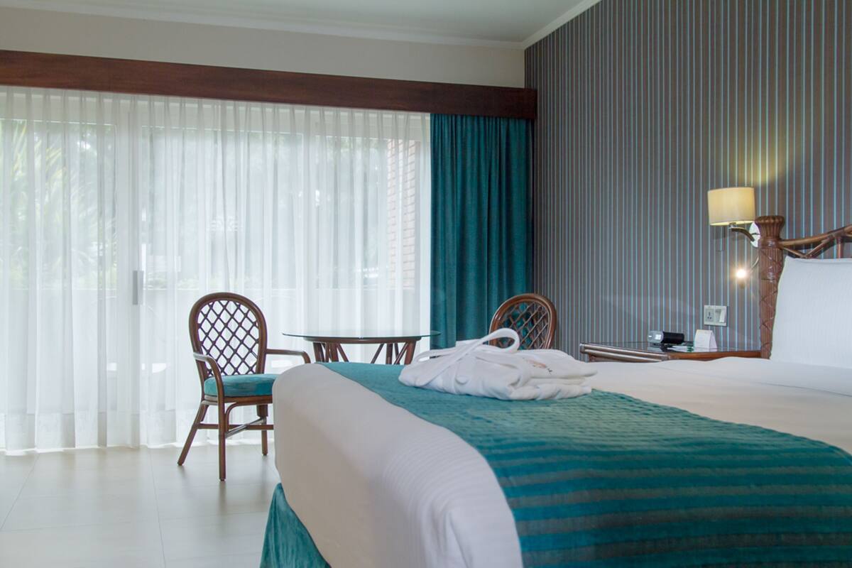 A hotel room with a bed, a chair, a table, and a lamp.