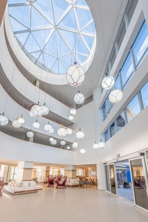 Relax in a spacious interior with a high ceiling and large skylight, surrounded by comfortable seating and a unique curved wall.