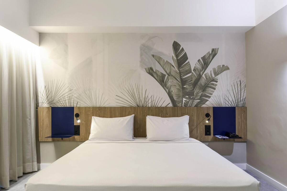 A modern bedroom with a large bed, wooden headboard, and a wall mural of foliage.