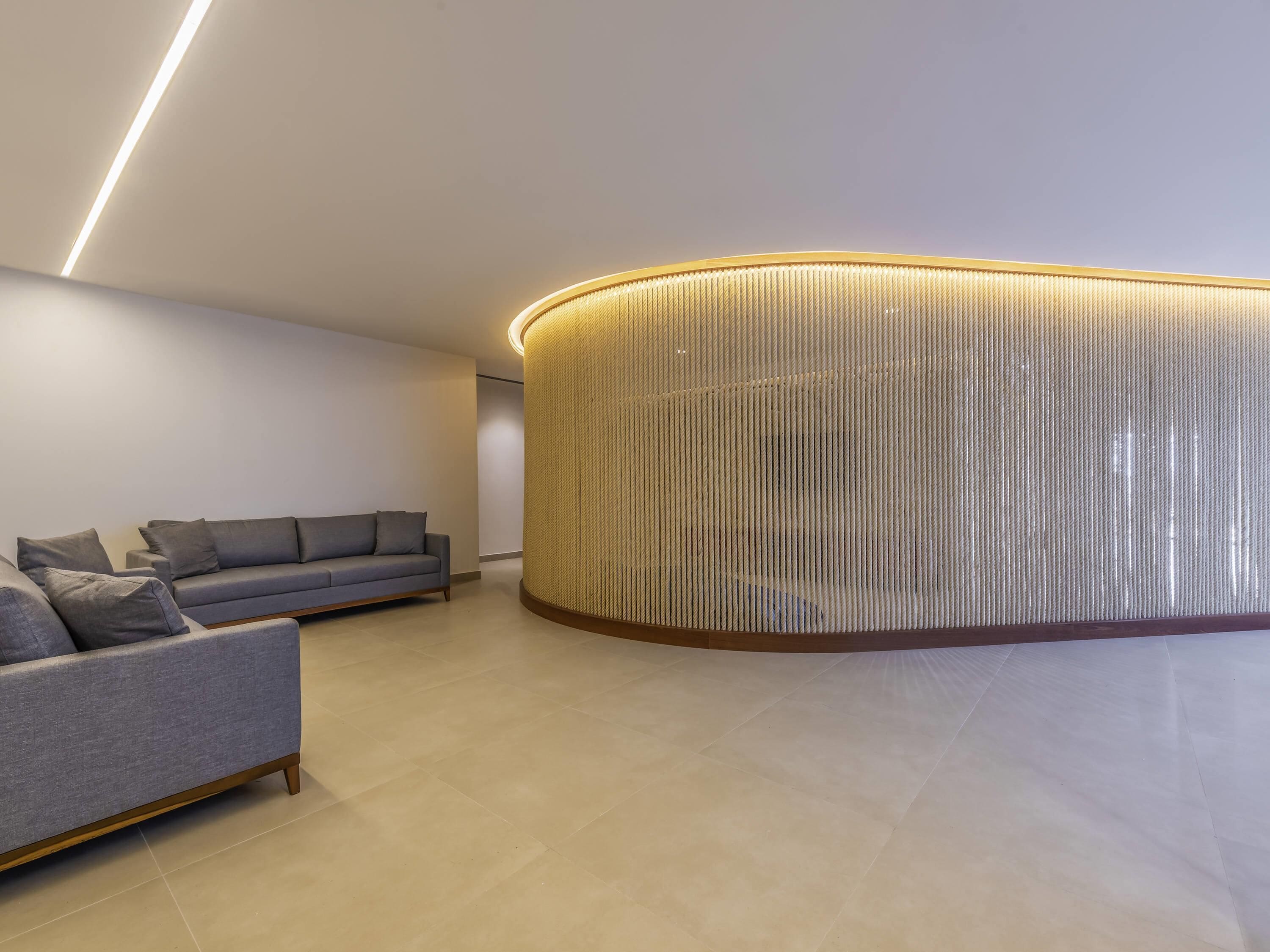 Un interior moderno con un sofá gris, una pared cilíndrica con textura y un diseño limpio y minimalista.