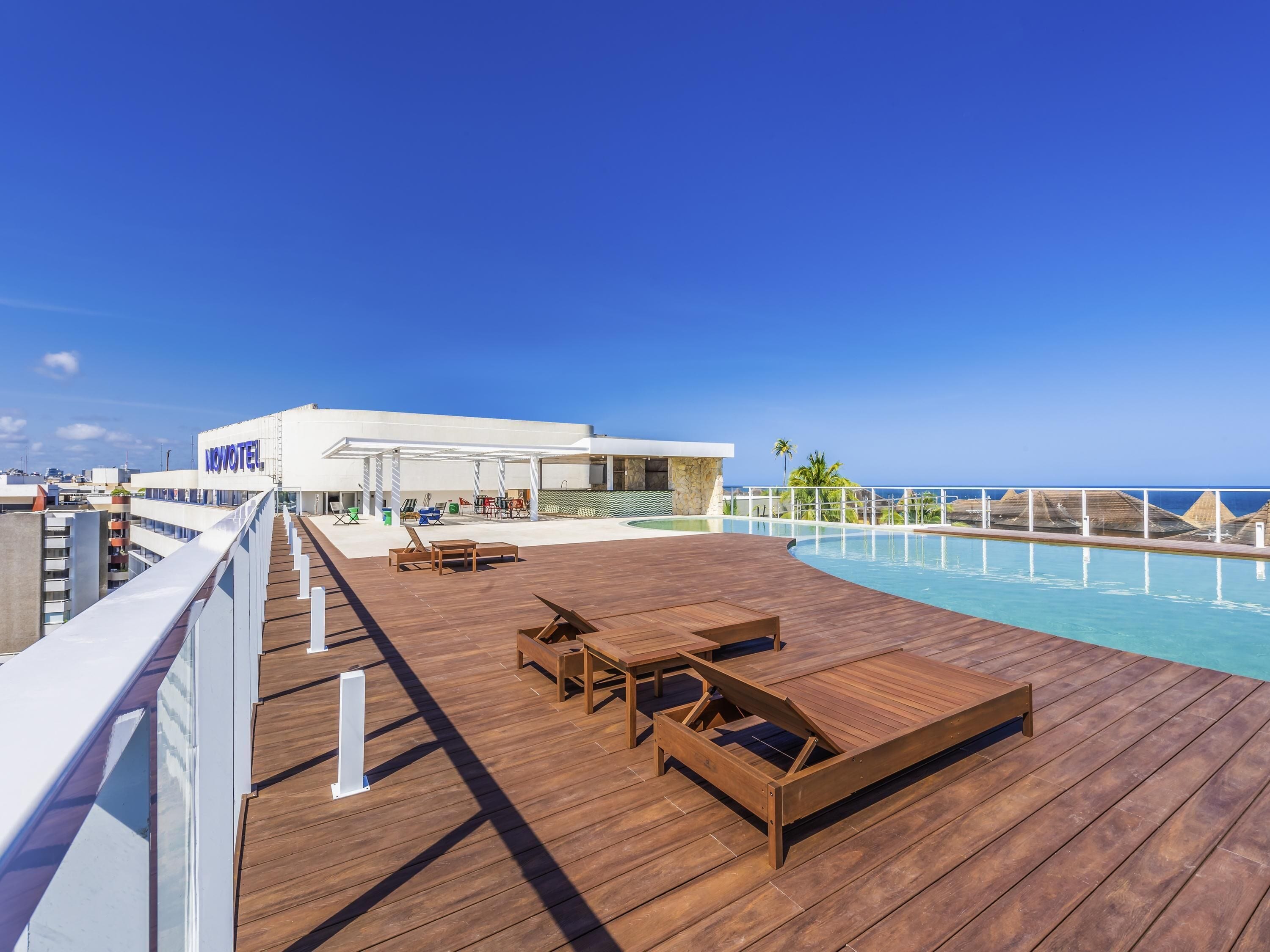 A poolside area with wooden loungers, a covered seating area, and a view of the ocean.