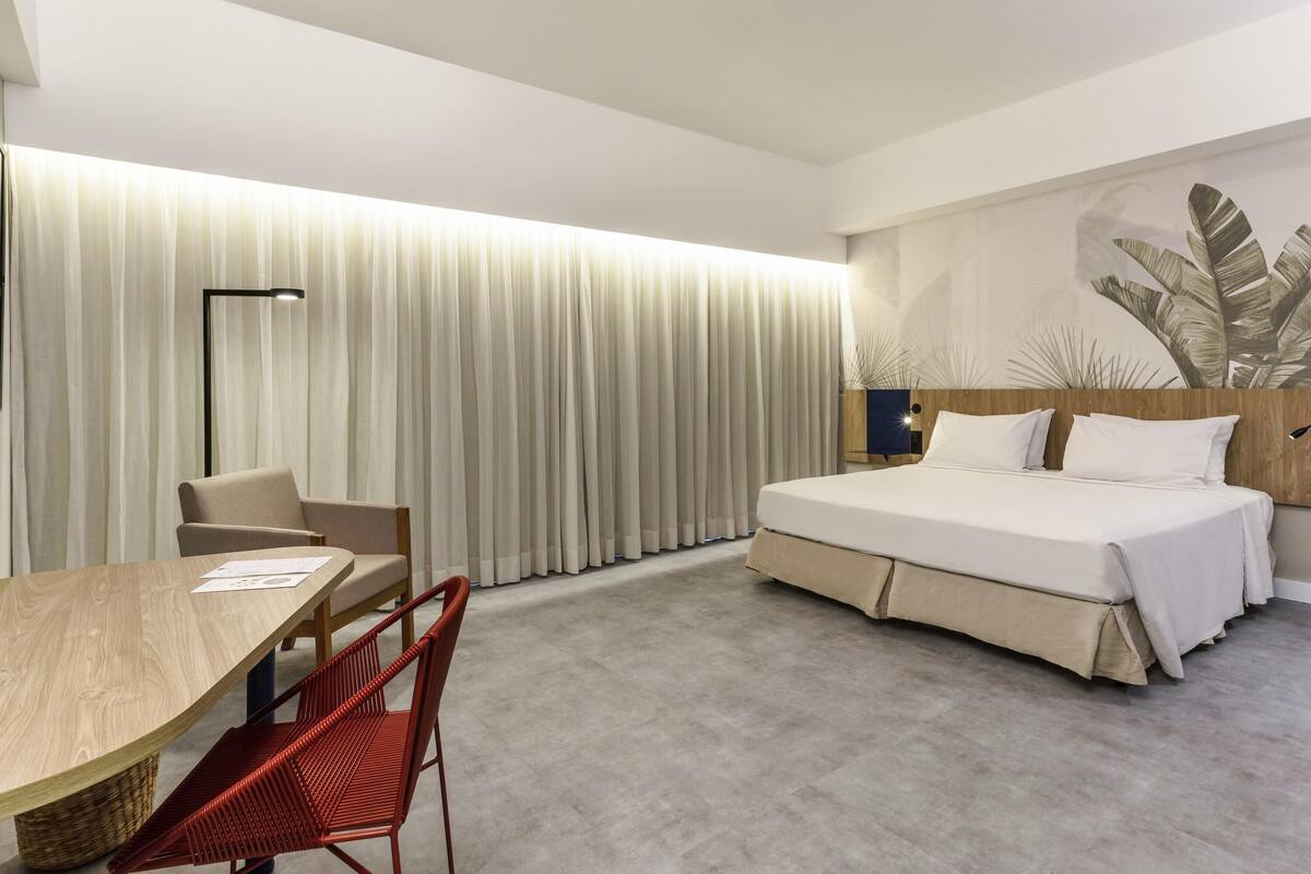 A modern hotel room with a large bed, a desk, and a chair.