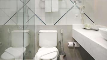 Un baño moderno con cabina de ducha de vidrio, inodoro, bidé y tocador con artículos de aseo.