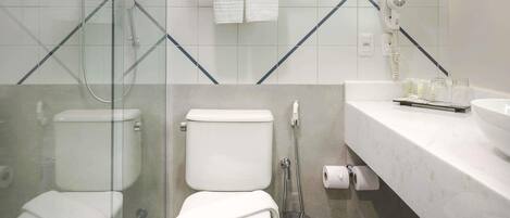 A modern bathroom with a glass shower enclosure, a toilet, a bidet, and a vanity with toiletries.