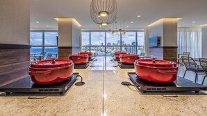 A modern hotel lobby with a view of the cityscape through large windows, a central chandelier, and multiple red hot tubs. - Novotel Salvador Rio Vermelho (Salvador)