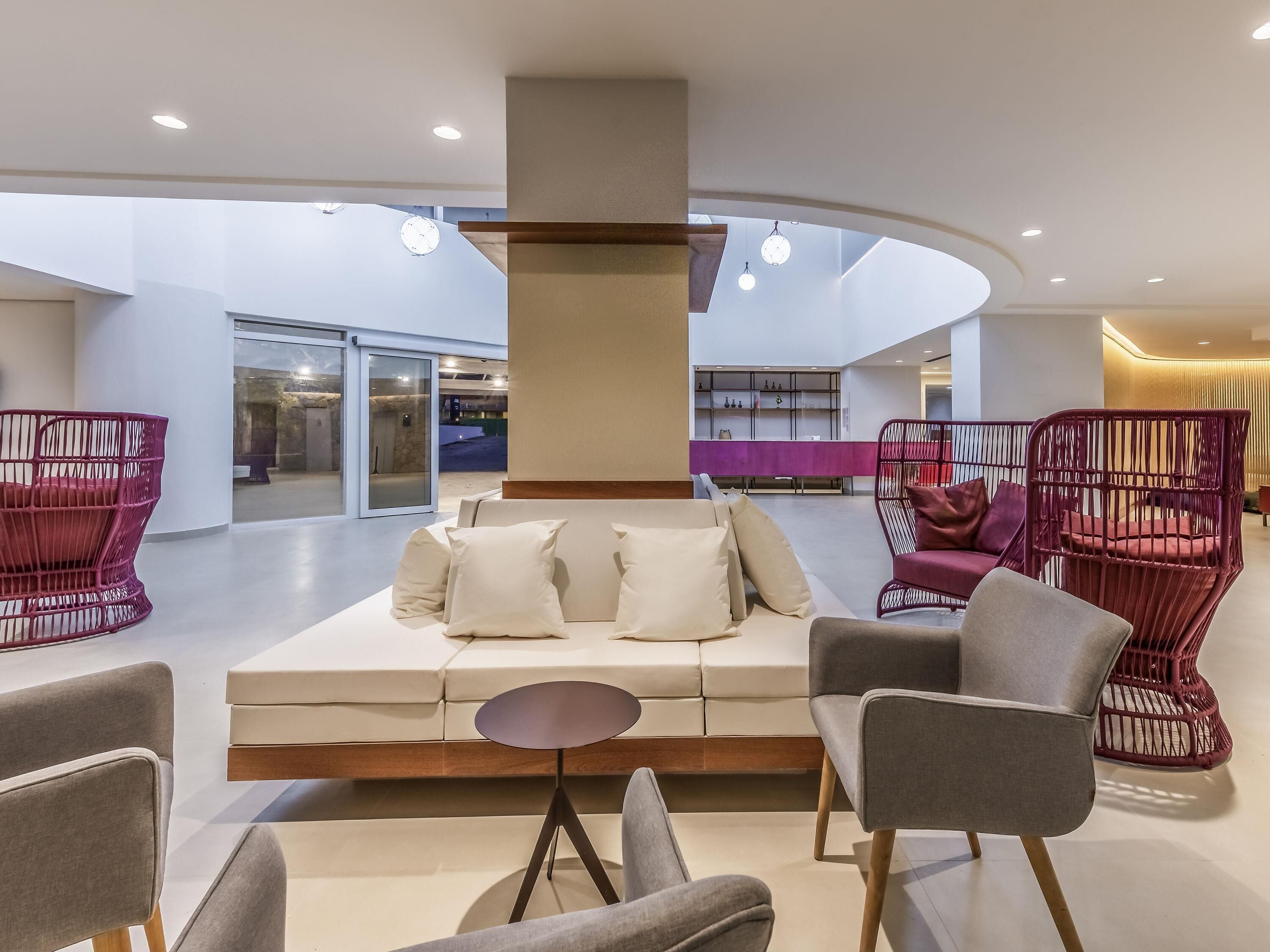 A modern lobby with a central seating area, a glass wall, and a reception desk.