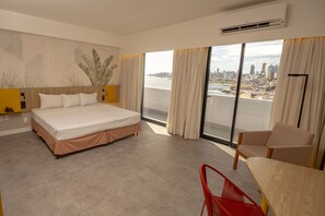 Relax in a spacious room with a large bed, a sliding glass door leading to a balcony with city views, and a dining area with a table and chair.