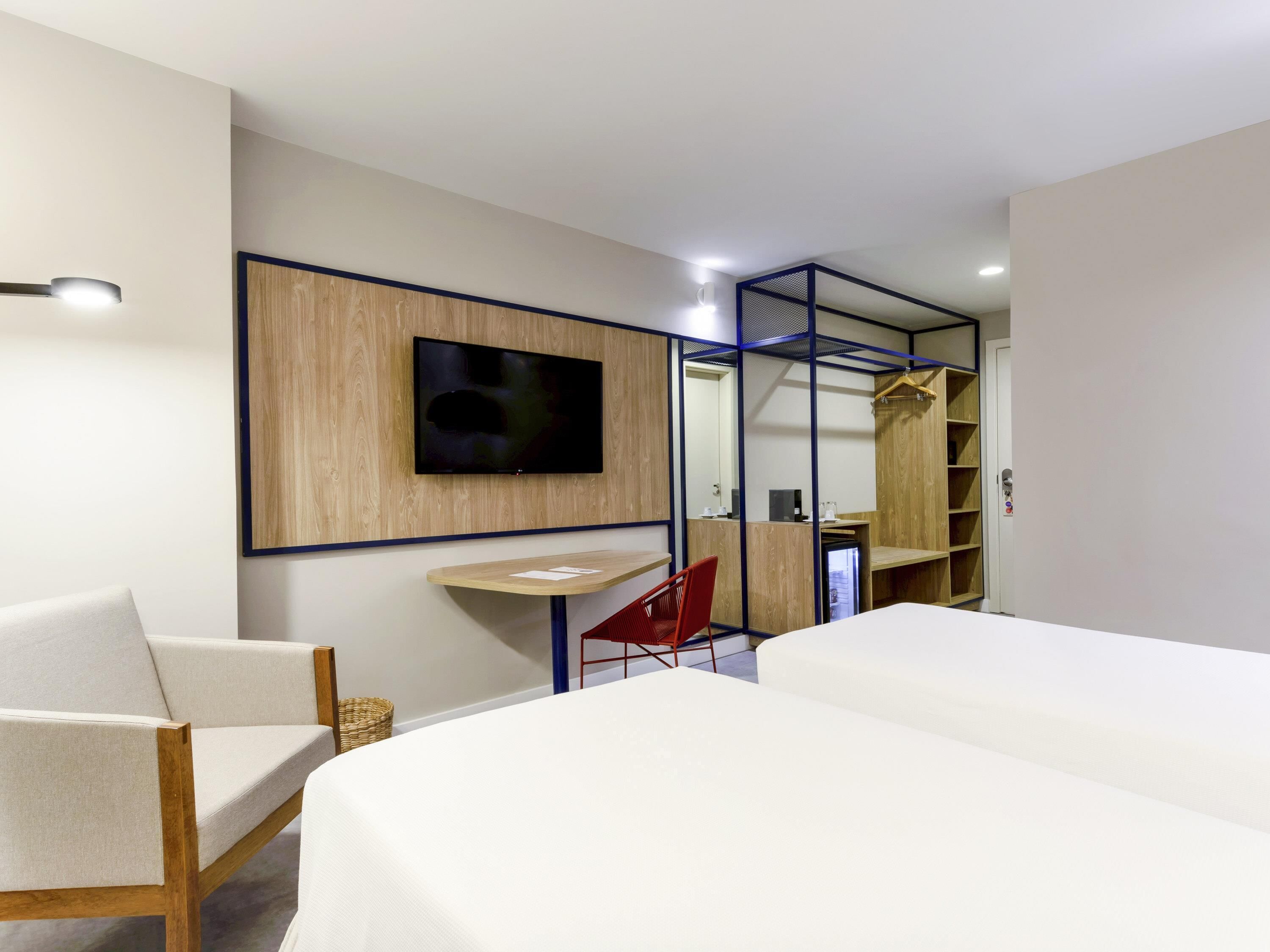 Une chambre d’hôtel moderne équipée d’un lit, d’un bureau, d’une chaise, d’un téléviseur fixé au mur et d’une armoire.