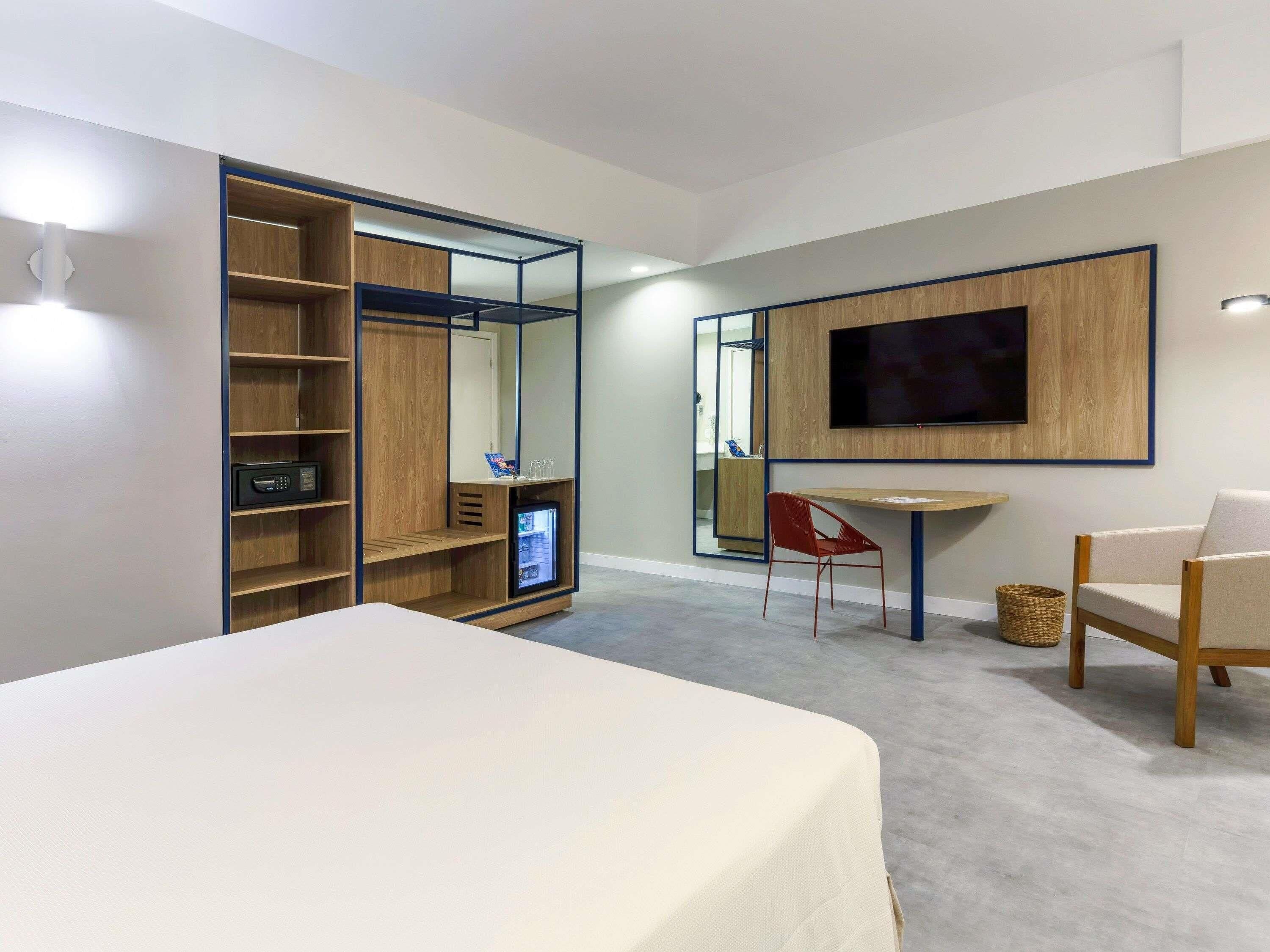 Una habitación de hotel moderna con una cama, un escritorio, una silla, un televisor y un armario con estantes.