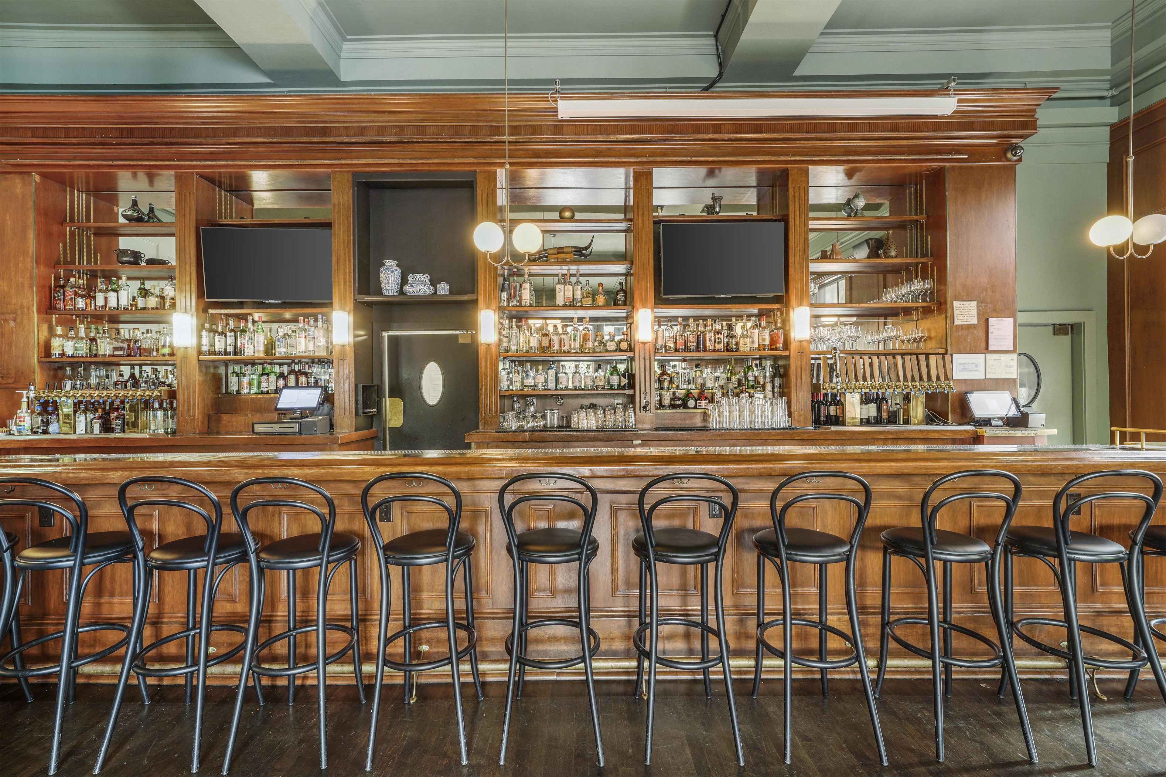 Zona de bar con paneles de madera, varias estanterías llenas de botellas y taburetes negros.