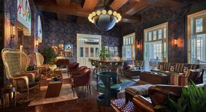 A spacious living area with a large globe chandelier, patterned wallpaper, and a variety of seating options including wicker chairs and sofas. - Graduate by Hilton Berkeley (Berkeley)
