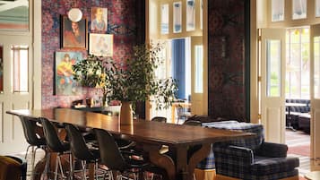 A dining area with a wooden table and chairs, a potted plant, and a patterned wall.