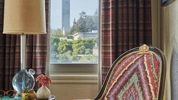 Una silla con tela estampada, una lámpara y una vista de una torre a través de una ventana con cortinas.