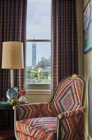 A chair with a patterned fabric, a lamp, and a view of a tower through a window with curtains. - Graduate by Hilton Berkeley (Berkeley)