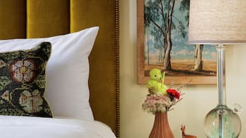 Uma cama com cabeceira, uma mesa de cabeceira com abajur, um vaso com flores e um quadro na parede.