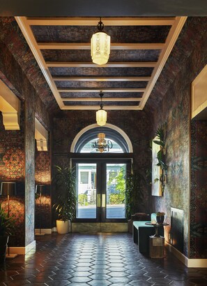 A hallway with patterned walls, a tiled floor, a chandelier, and a door leading outside. - Graduate by Hilton Berkeley (Berkeley)