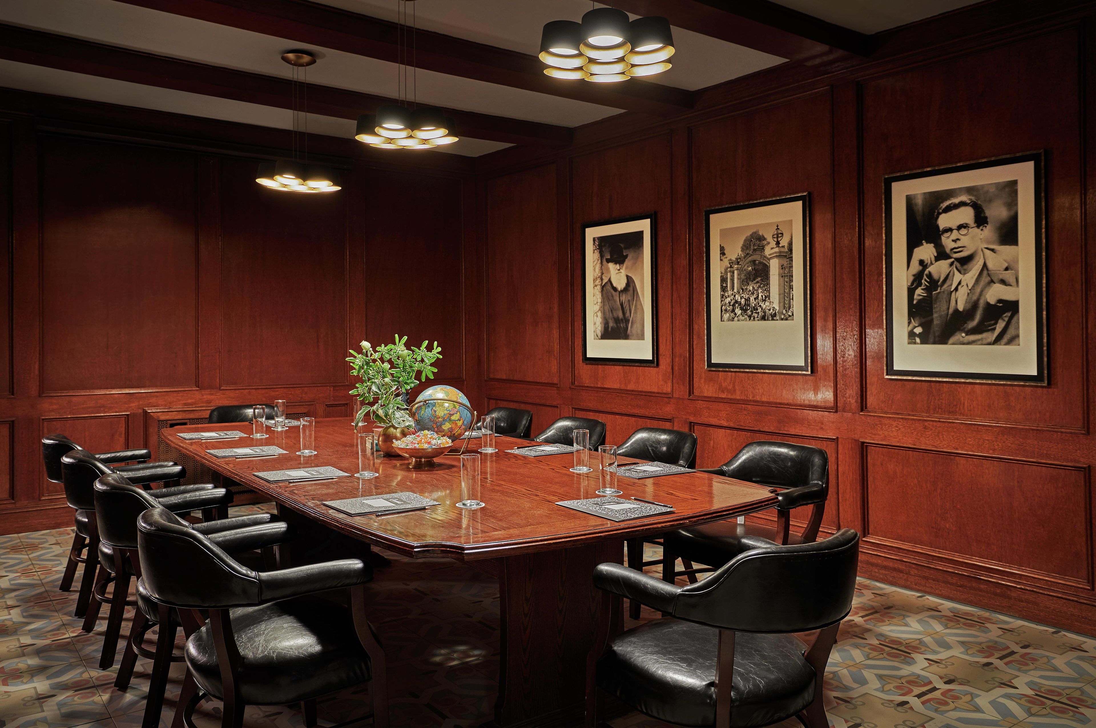 A conference room with a long table, black leather chairs, framed pictures on the walls, and a globe on the table.