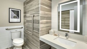 A modern bathroom with a toilet, a handrail, a sink, and a mirror.
