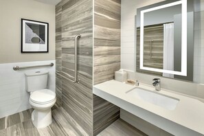 A modern bathroom with a toilet, a handrail, a sink, and a mirror.