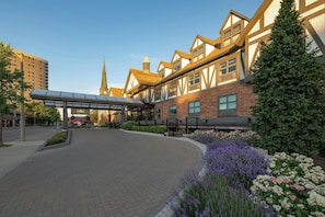 A hotel entrance with a covered walkway, brick facade, and surrounding greenery.
