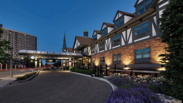 A hotel with a traditional architectural style, featuring a prominent entrance with a covered walkway, a brick facade, and a landscaped garden area. - The Insignia Hotel, Sarnia, a Tribute Portfolio Hotel (Sarnia)