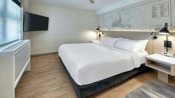A modern hotel room with a large bed, a flat-screen TV mounted on the wall, a ceiling fan, and a map of the city on the wall.