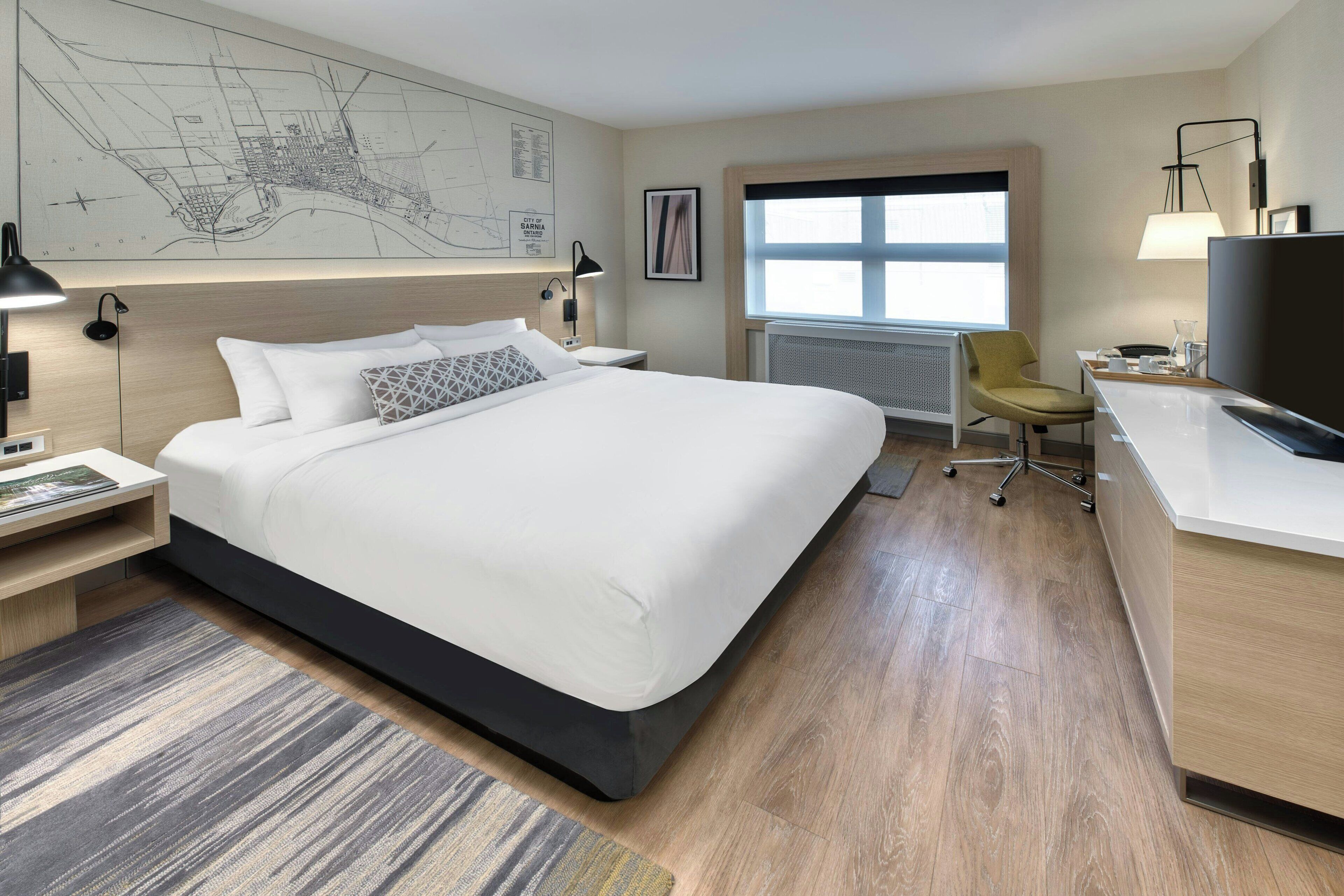 Una habitación de hotel moderna con una cama grande, un escritorio, una silla y un mapa en la pared.