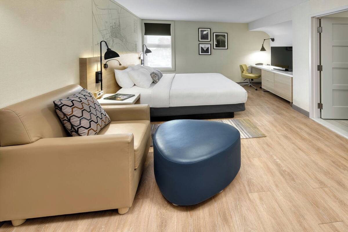 A modern hotel room with a bed, a sofa, a desk, and a TV.