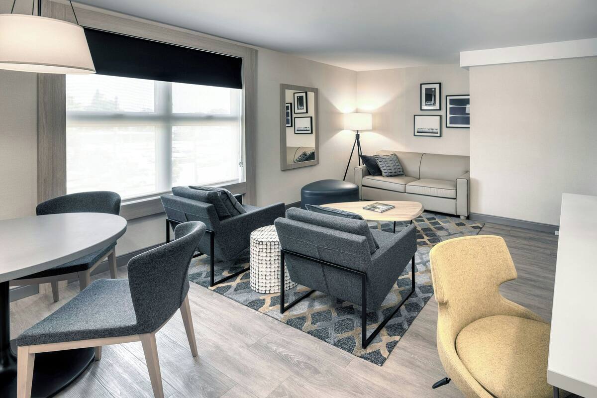 A modern living room with a round table, grey and yellow chairs, a sofa, and a lamp.