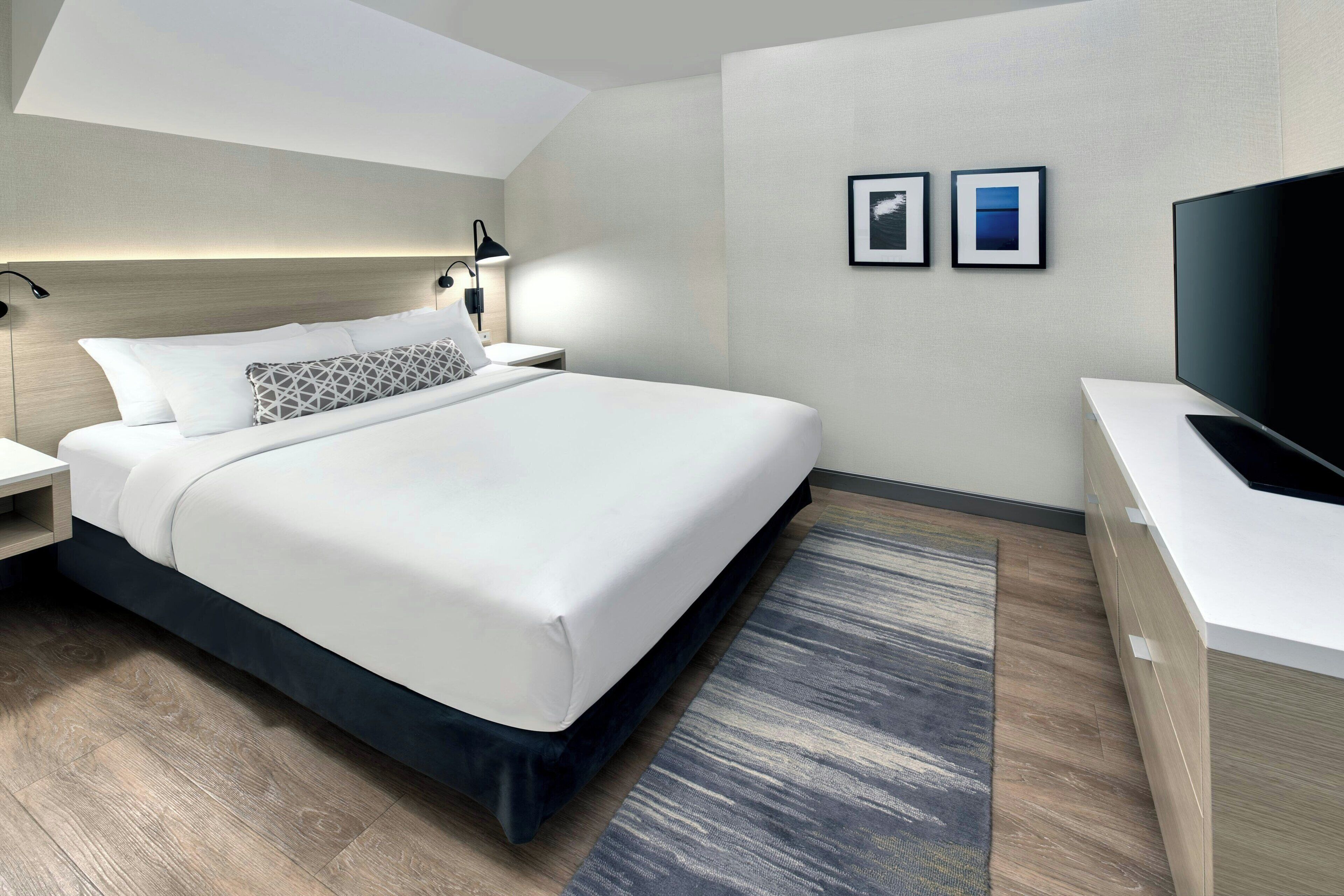 A modern hotel room with a large bed, bedside tables, a flat-screen TV, and a small desk.