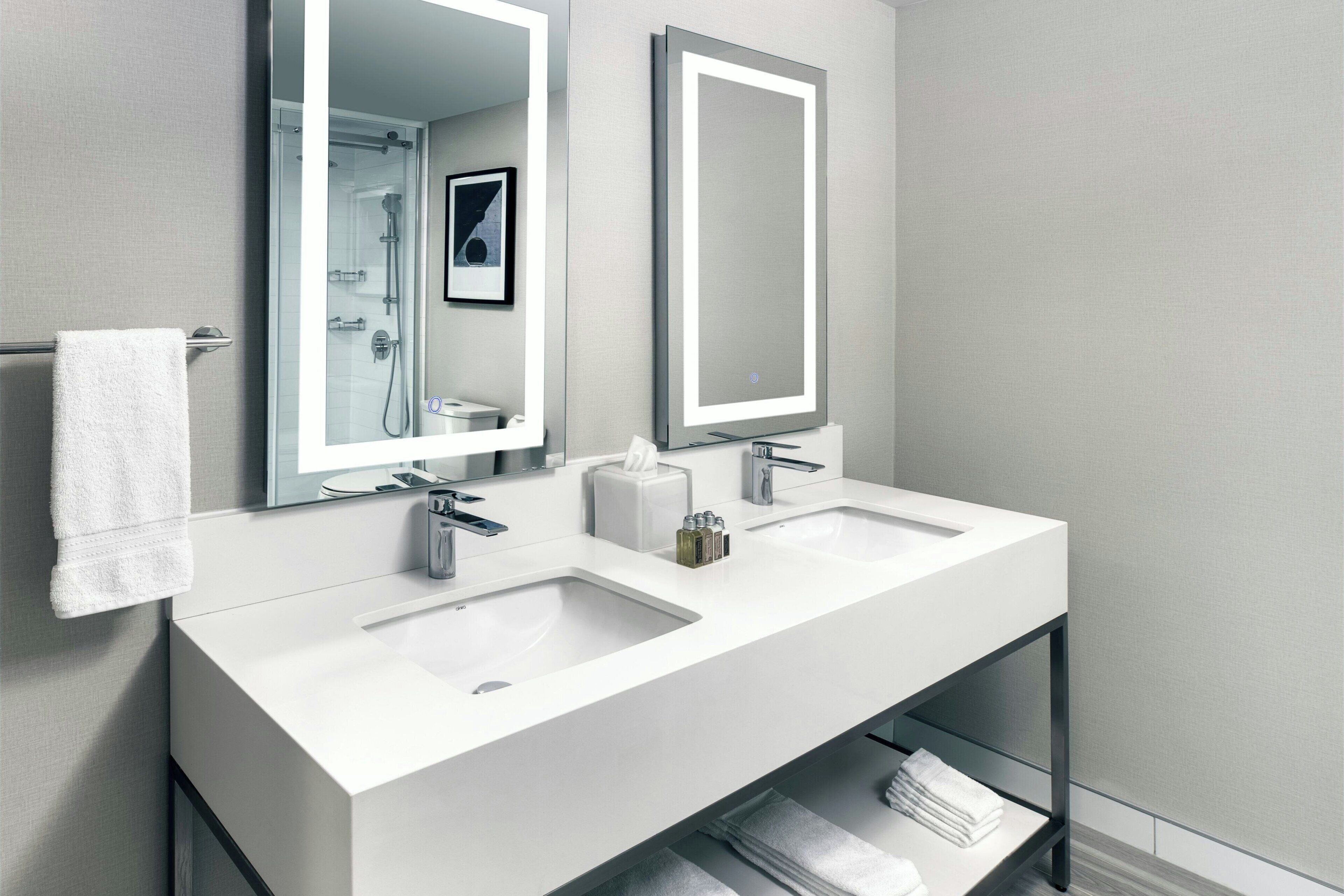 A modern bathroom with two sinks, a large mirror, and a towel rack.