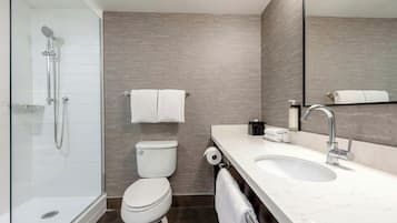 Un baño moderno con ducha envuelta en vidrio, inodoro, lavamanos con espejo y un perchero para toallas.