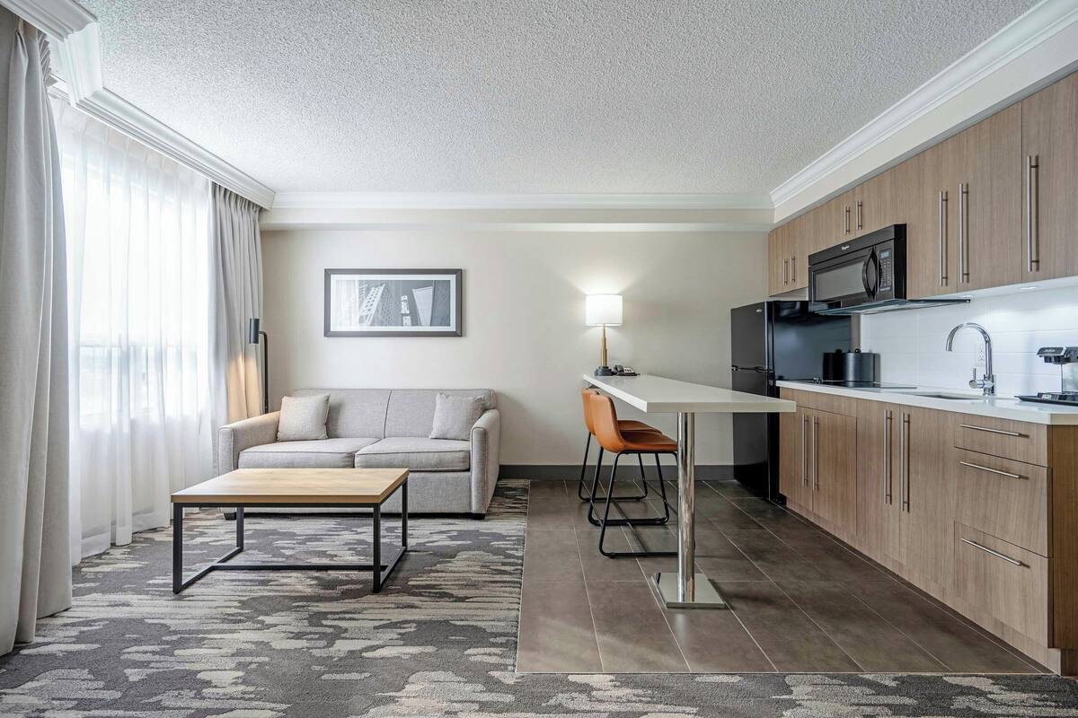 A modern kitchen with wooden cabinets, a microwave, and a sink. There is a dining area with a table and chairs.
