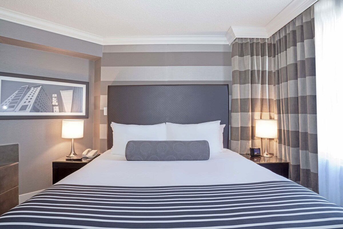A hotel room with a large bed, two bedside tables with lamps, a headboard, and a framed picture on the wall.