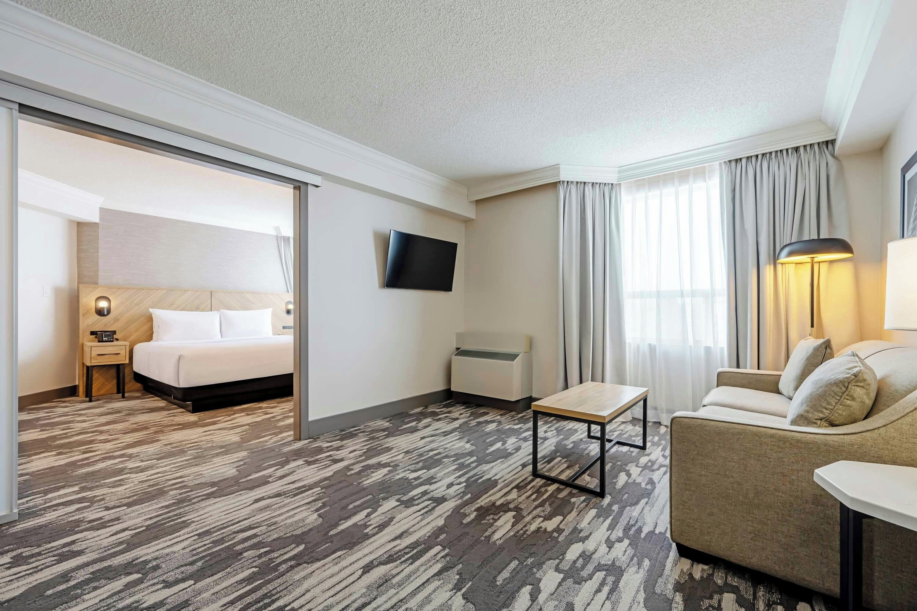 Une chambre d’hôtel avec un lit, un canapé, une télévision, une lampe et une petite table.