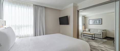 A hotel room with a large bed, a flat-screen TV mounted on the wall, a sofa, and a door leading to another room.