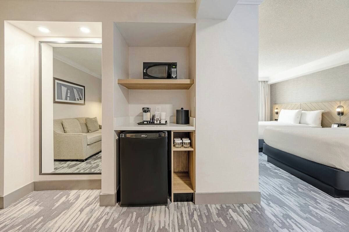 A compact hotel room with a kitchenette, a bed, and a small seating area.