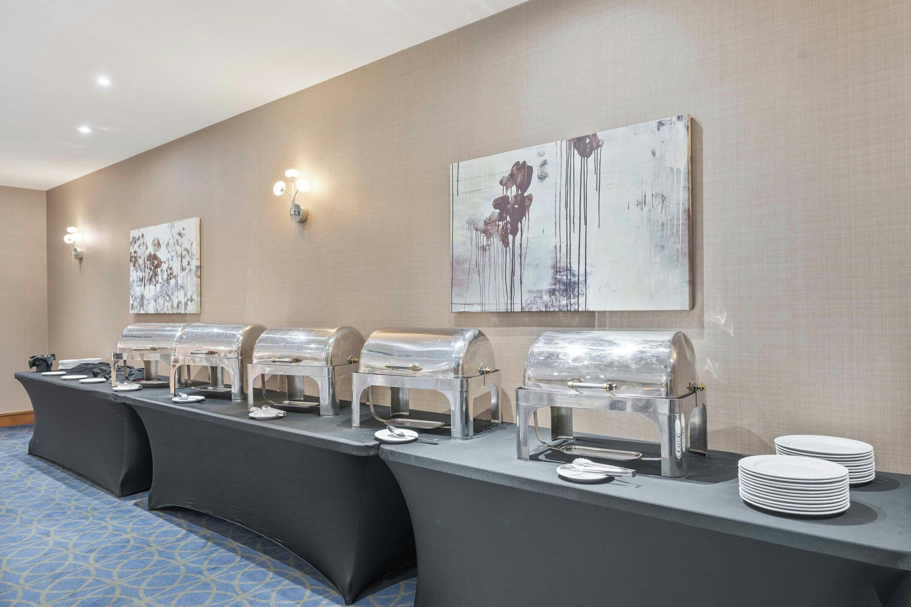 A buffet setup with multiple self-service stations, wall-mounted artwork, and a patterned carpet.