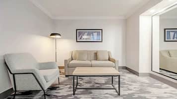 Una sala de estar moderna con un sillón gris, un sofá color beige y una mesita de centro de madera. Se observa una lámpara de pie y un cuadro en la pared.