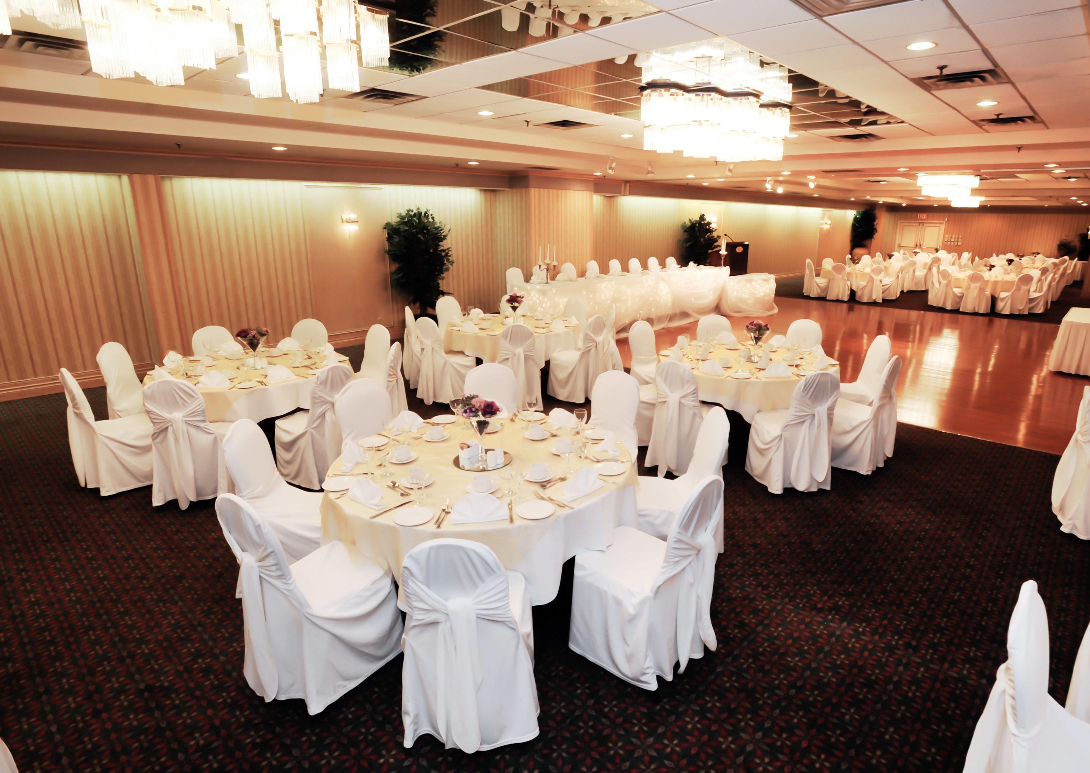 A banquet hall with round tables, white chairs, and chandeliers.