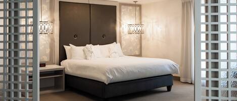 A modern hotel room with a large bed, a nightstand, and two wall-mounted lamps.