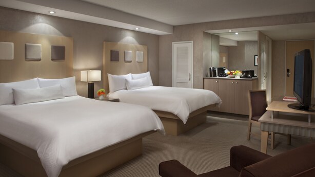 Een hotelkamer met twee bedden, een bureau, een stoel, een televisie en een kitchenette.