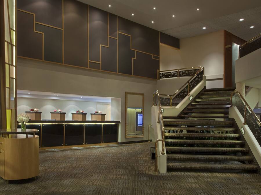 A hotel lobby with a grand staircase, a reception desk, and a large mirror.