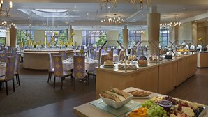 Een ruime eetruimte met ronde tafels, stoelen en een buffet met diverse gerechten.