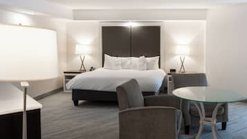 Una habitación de hotel con una cama, dos mesitas de noche con lámparas, una mesa de vidrio y dos sillones.