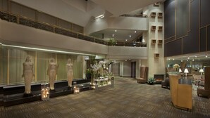 Een ruime lobby met een hoge plafond, een centraal zitgedeelte en een decoratieve presentatie van vazen en kaarsen.