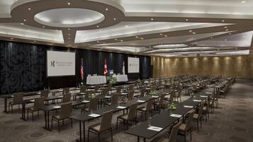 A conference room with multiple tables and chairs, a stage with a podium, and flags.